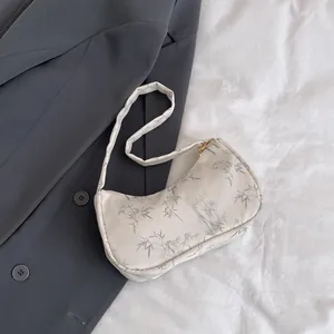 Close-up of cream shoulder bag with grey bamboo leaf print and gold zipper detail