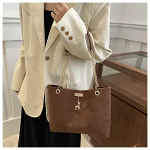 Detail of dark brown suede shoulder bag with gold chain strap and deer charm on a model