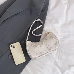 Detail of white crescent underarm bag with grey bamboo leaf print and gold hardware