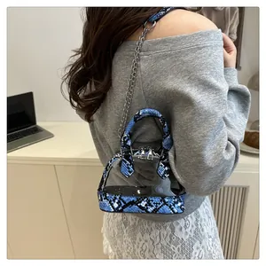 Dettaglio di una borsa a conchiglia in PVC trasparente con finiture in pelle pitonata blu e catena