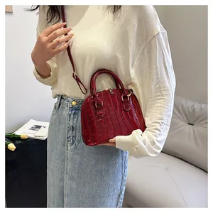 Detail of burgundy crocodile pattern shell bag with golden hardware on a shoulder