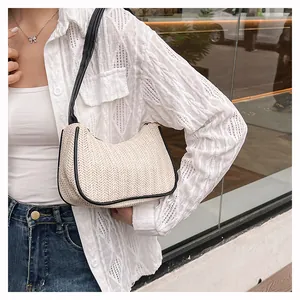 Detail of woven straw underarm bag featuring black leather trim and fishbone pattern
