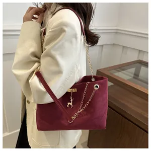 Close-up of vintage burgundy suede shoulder bag with gold chain and deer pendant detail