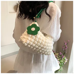 Détail du sac cylindrique blanc à texture bulles avec pendentif fleur verte sur l'épaule