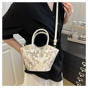 Detail of white cross-body bag featuring floral embroidery and gold hardware accents