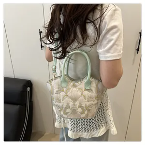Detail of floral embroidery on a white crossbody bag with green ring handle and strap