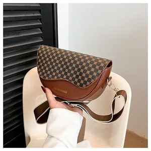 Close-up of saddle bag with geometric dot print, gold logo, and wide fabric strap