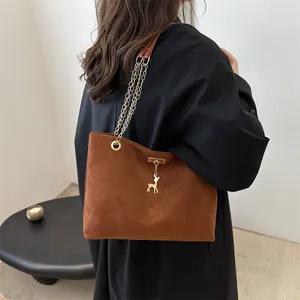 Brown faux suede tote bag with golden chain strap and deer pendant in a minimalist interior