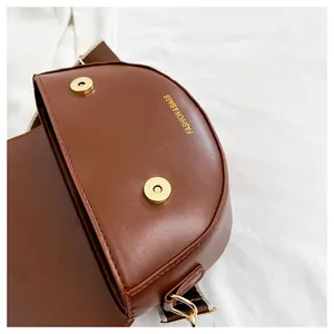 Detail of brown PU leather saddle bag showing gold magnetic closure and wide woven strap