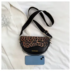 Compact leopard print saddle bag with wide strap shown next to a phone for size scale