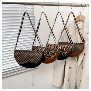 Detail of half-moon saddle bags with leopard print, wide striped strap and zipper close