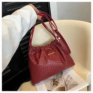 Détail de la texture tressée du sac bordeaux avec logo doré posé sur une chaise moderne