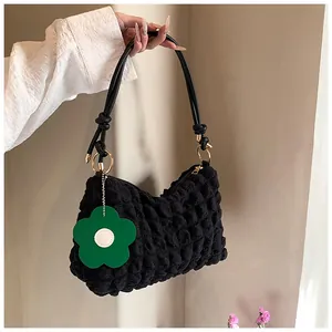 Détail du sac cylindre noir en tissu gaufré avec bandoulière en cuir et breloque fleur
