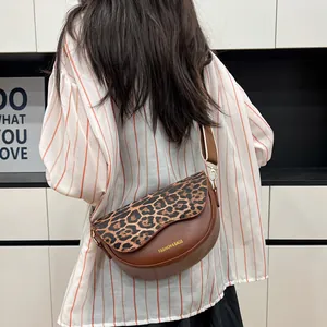 Brown leather saddle bag with leopard print flap and wide strap worn by a model