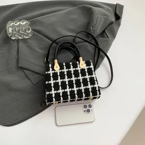 Classic black and white tweed crossbody bag with woven handles on a grey blazer background