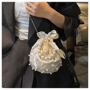 Schicke elfenbeinfarbene Satin-Beuteltasche mit Perlen und Kettenriemen am Modell getragen