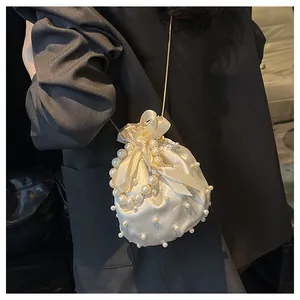 Detailansicht der cremefarbenen Satin-Beuteltasche mit Perlen auf dunklem Blazer