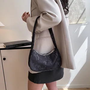 Detail of minimalist black underarm bag with bamboo leaf print on a casual blazer model