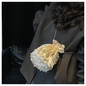 Detailansicht der cremefarbenen Satin-Beuteltasche mit Perlenbesatz und Schleifendekoration