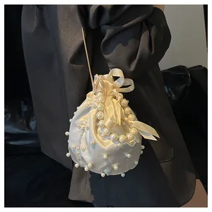 Detailaufnahme der beigen Satin-Beuteltasche mit Perlenverzierung und einer Schleife