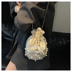 Detail einer cremefarbenen Satin-Beuteltasche mit Perlenverzierung und Kettenriemen