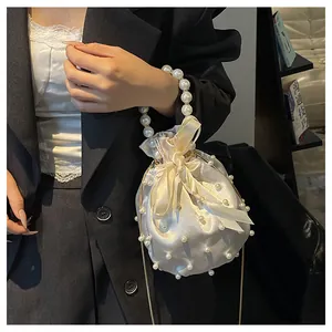 Detail der cremefarbenen Satin-Beuteltasche mit Perlenverzierung und Seidenschleife