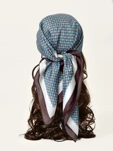 Dettaglio di un foulard in seta blu con motivo a catena e bordo marrone sui capelli