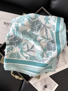 Detailed view of white silk scarf with teal floral pattern and twill border on tray