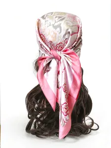 Dettaglio di un foulard floreale in seta rosa annodato sui capelli con effetto lucido