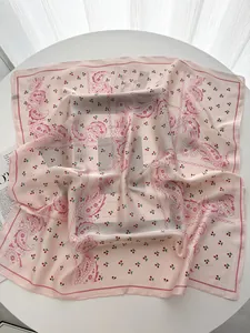 Detailed view of a pink silk scarf featuring paisley patterns and cherry prints on a white table