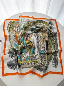 Macro detail of leaf and feather print silk scarf with luxury orange border on a table