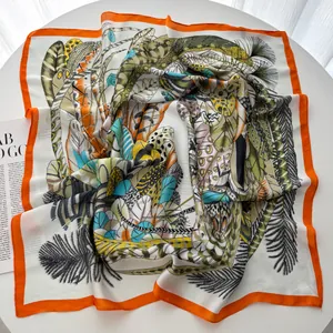 Detailed view of leaf print silk scarf with bright orange border on a white table