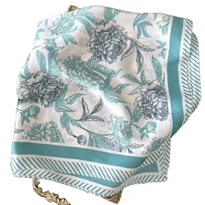 Elegant silk-like scarf with green floral pattern on white base, displayed on gold tray