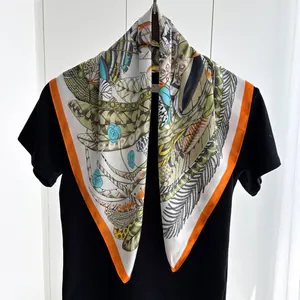 Silk-feel square scarf with leaf print and vibrant orange border on black shirt