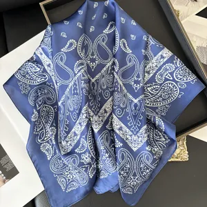 Détail d'un foulard en soie bleu marine avec motif paisley blanc sur un plateau élégant