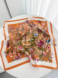 Détail du foulard en soie orange avec motifs floraux et papillons sur bordure blanche