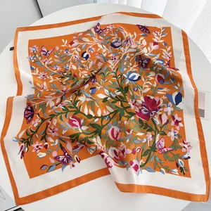Détail d'un foulard carré orange avec imprimé floral et papillons au fini soyeux