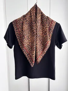 Dettaglio di foulard leopardato in seta sintetica con bordo rosso scuro su maglia nera