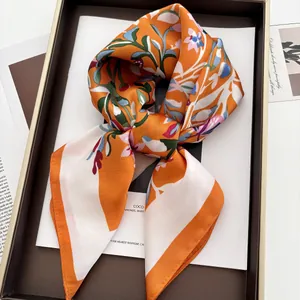 Détail d'un foulard en soie orange avec motif floral élégant dans son coffret cadeau
