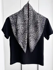 Dettaglio di un foulard quadrato con stampa leopardata in finta seta piegato su maglia nera