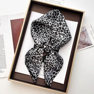 Dettaglio macro di foulard in seta con stampa leopardata e bordi arrotolati grigi in scatola