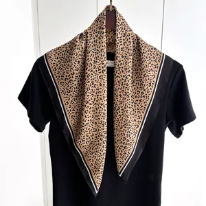 Dettaglio di un foulard in seta con stampa leopardata e bordi neri su gruccia in legno