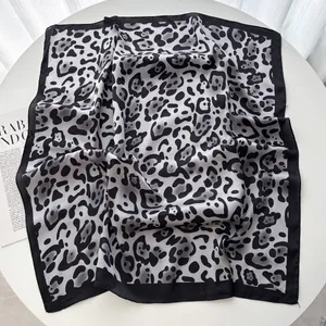 Dettaglio di un foulard quadrato in raso leopardato con bordi neri su un tavolo bianco