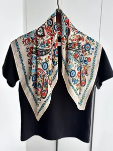Détail d'un foulard en soie à motif paisley crème avec des accents rouges et bleus vifs
