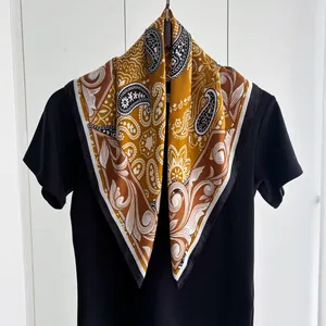 Dettaglio di un foulard in seta gialla con motivo paisley vintage e bordi neri fini