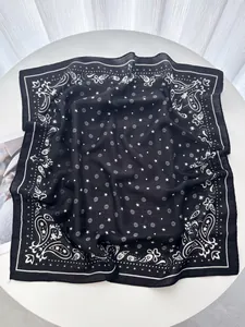 Detail of black paisley silk scarf featuring star and floral prints on a white table