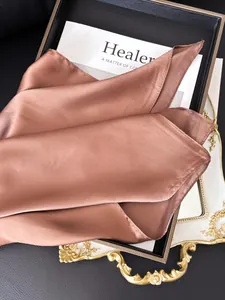 Détail d'un foulard en soie satinée bronze avec texture brillante sur un plateau