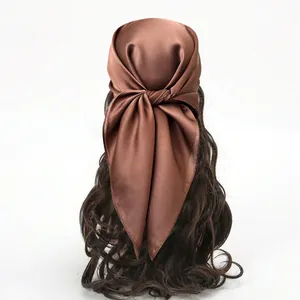 Détail d'un foulard en satin de soie marron chocolat attaché sur de longs cheveux ondulés