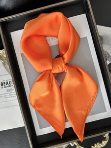 Détail d'un foulard en satin orange vif noué montrant une texture soyeuse et brillante