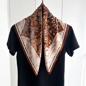 Dettaglio di sciarpa in seta con motivi paisley drappeggiata su una t-shirt nera